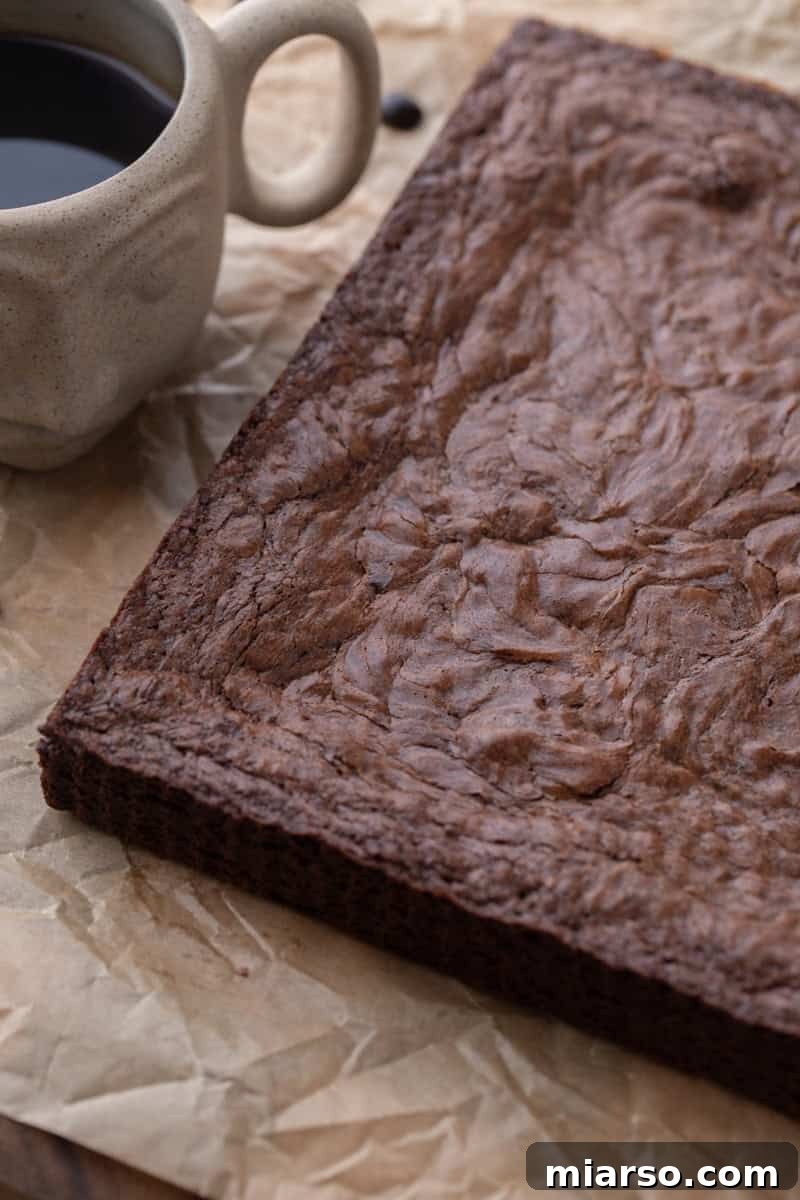 Espresso Fudge Brownies 12 Whole slab of baked brownies with crinkly top on parchment next to a cup of coffee