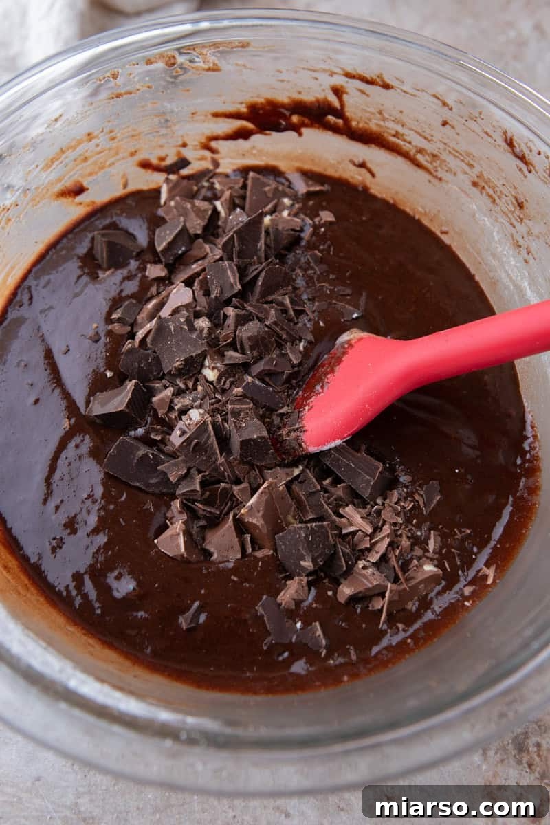 Espresso Fudge Brownies 10 Folding chopped dark chocolate chunks into brownie batter with a red silicone spatula