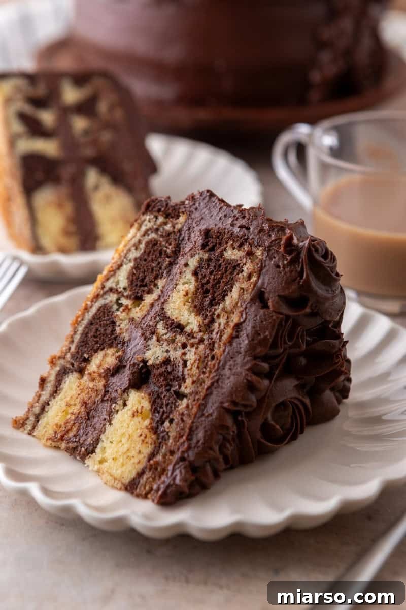 Ultimate Moist Marble Layer Cake with Rich Chocolate Cream Cheese Frosting 3 Slice of marble cake with chocolate frosting on a white scalloped plate with coffee in the background