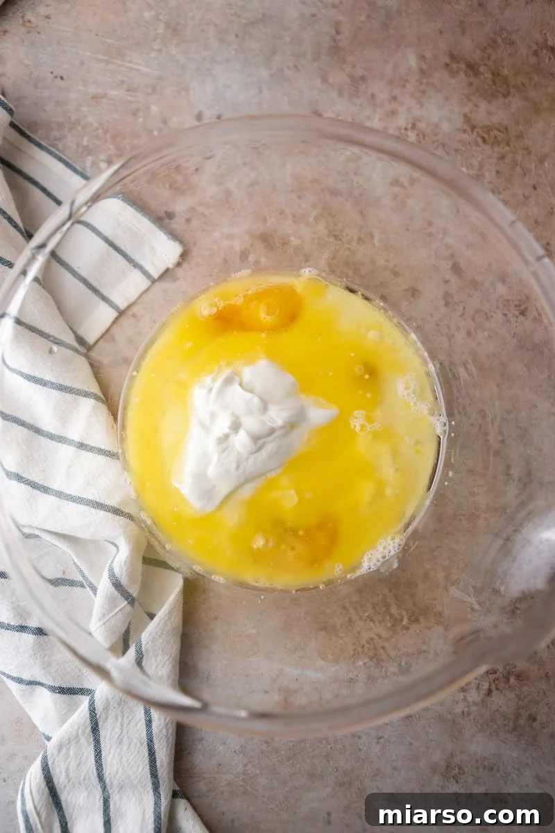 Ultimate Moist Marble Layer Cake with Rich Chocolate Cream Cheese Frosting 6 Eggs, melted butter, sour cream, and oil combined in a glass mixing bowl