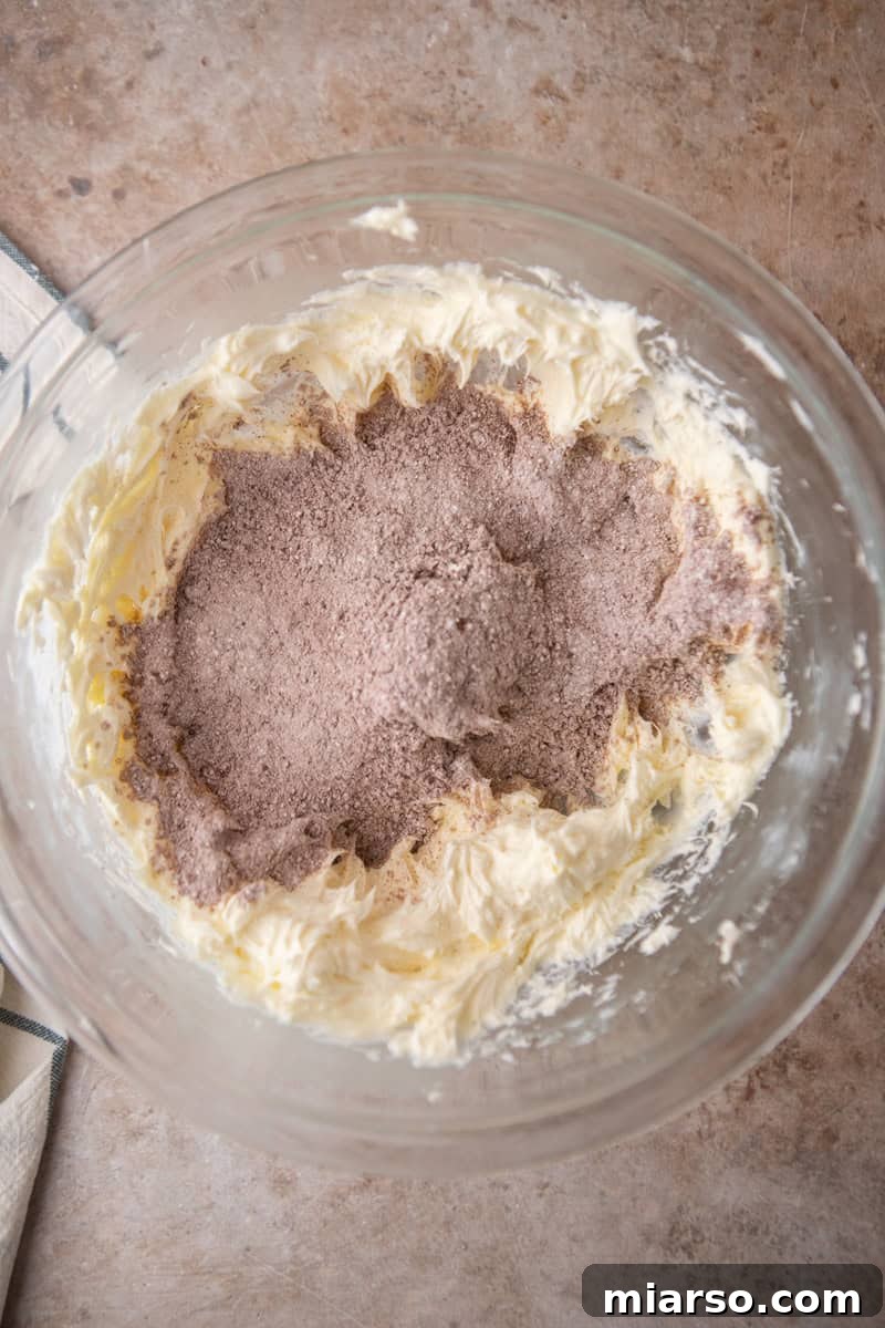Velvety Chocolate Cream Cheese Indulgence 5 Sifted cocoa powder and powdered sugar added to beaten cream cheese and butter in a glass bowl