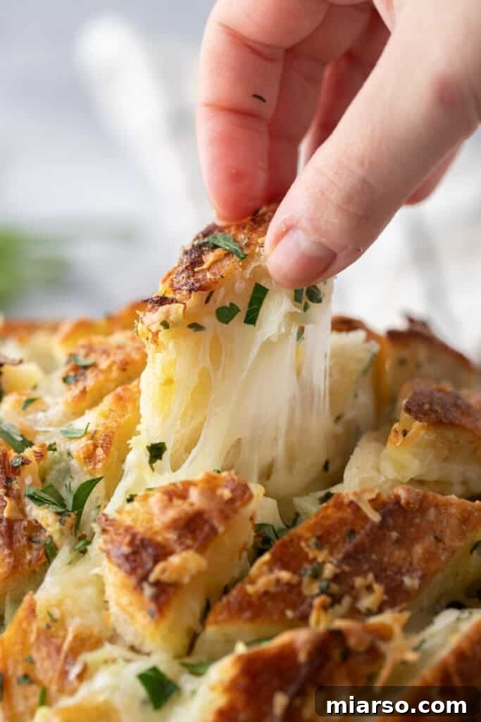 Hand pulling apart a piece of cheesy sourdough garlic bread with melted mozzarella stretching

