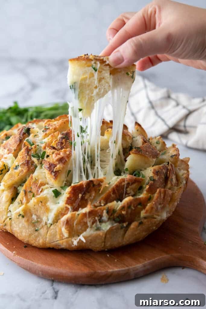 Hand pulling apart baked sourdough garlic bread with melted mozzarella stretching
