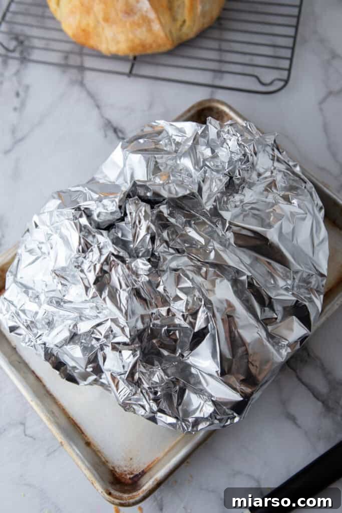 Garlic butter bread covered tightly with foil on baking sheet
