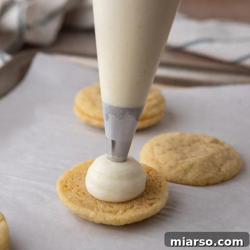 Cream cheese lemon frosting being piped onto a cooled lemon sugar cookie to make a sandwich.
