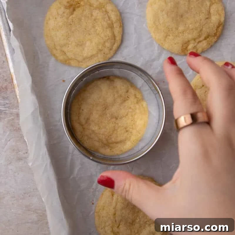 Round cookie cutter being used to swish a freshly baked lemon cookie back into a perfect circle.