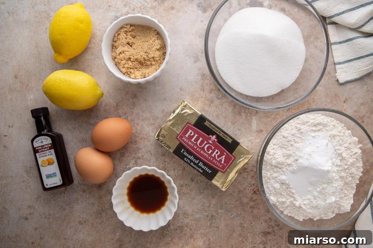 Overhead flatlay of lemon sandwich cookie ingredients including Plugrà butter, lemons, eggs, sugar, flour, and lemon extract.