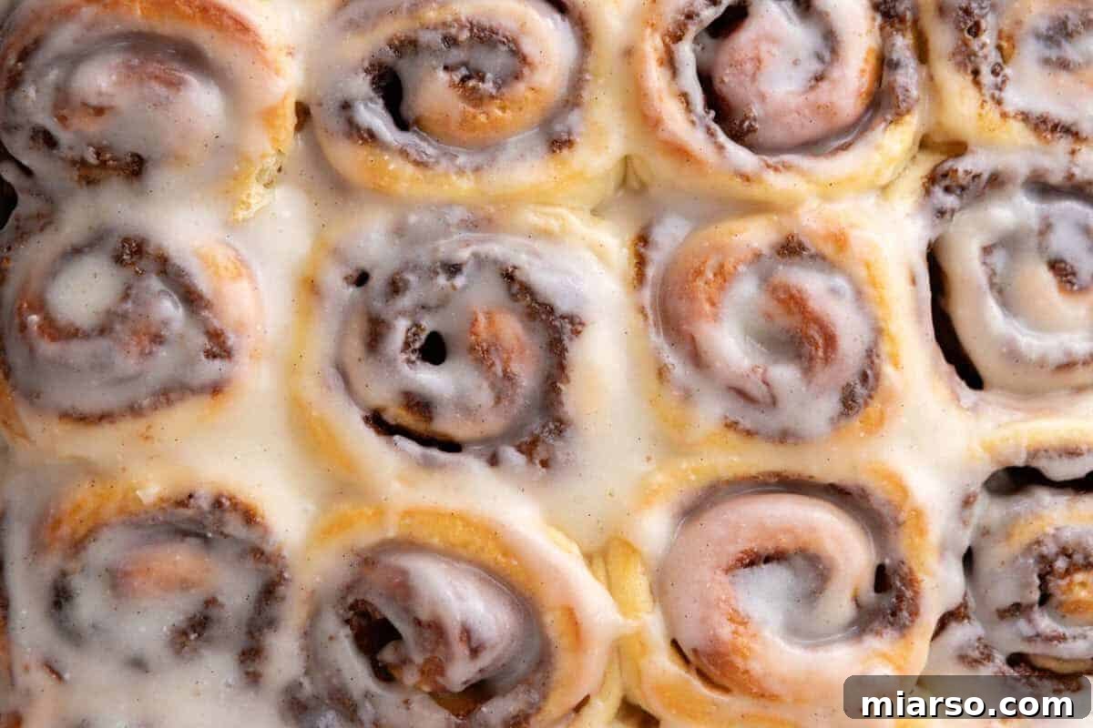 Mini cinnamon rolls with cream cheese glaze in a baking pan, close up showing visible cinnamon swirls