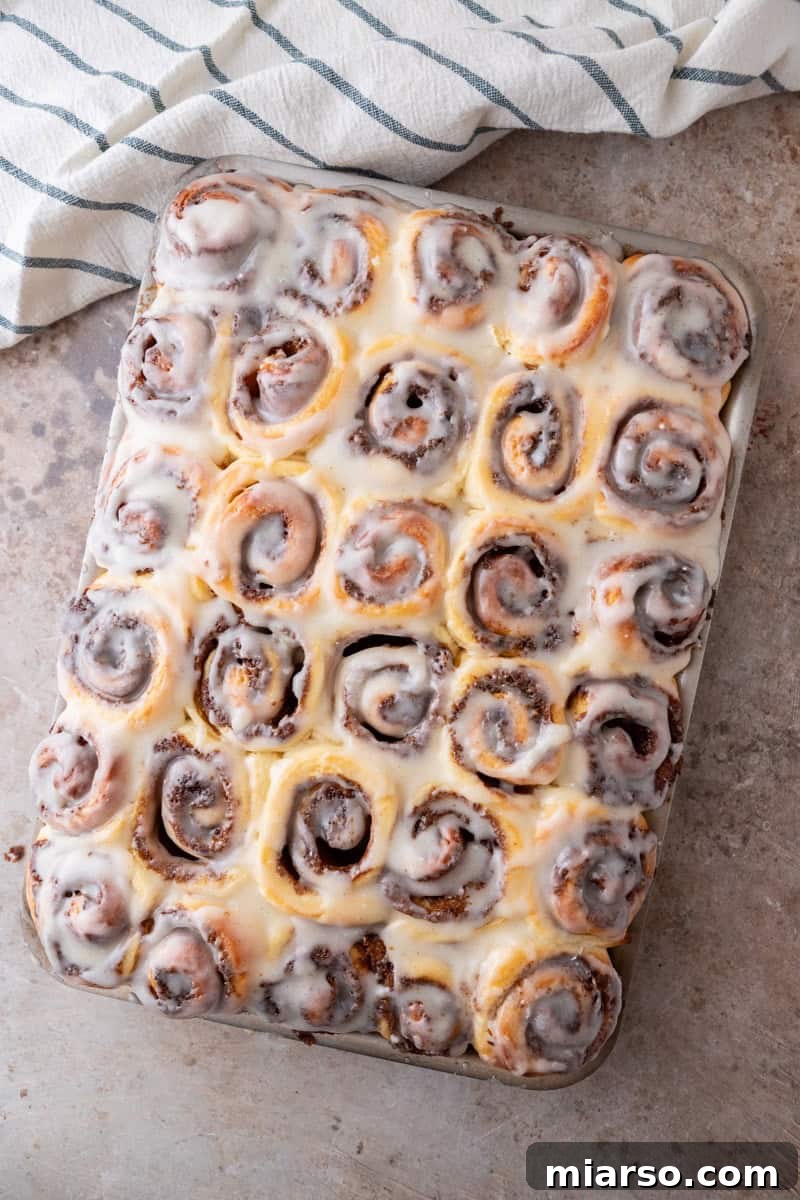 Mini cinnamon rolls with thin cream cheese glaze drizzled over the top in a sheet pan