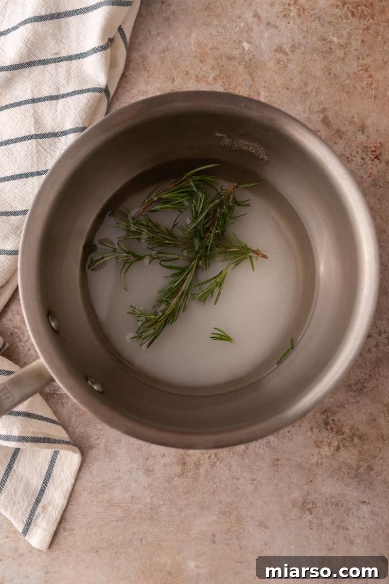 Fresh rosemary sprigs steeping in sugar and water in a saucepan before simmering