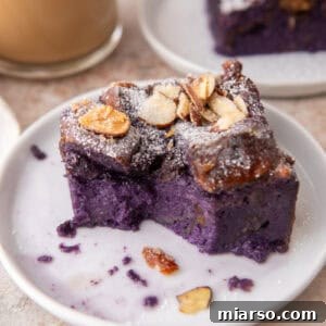 Ube French toast bake slice on a small white plate dusted with powdered sugar and toasted almonds with coffee in the background