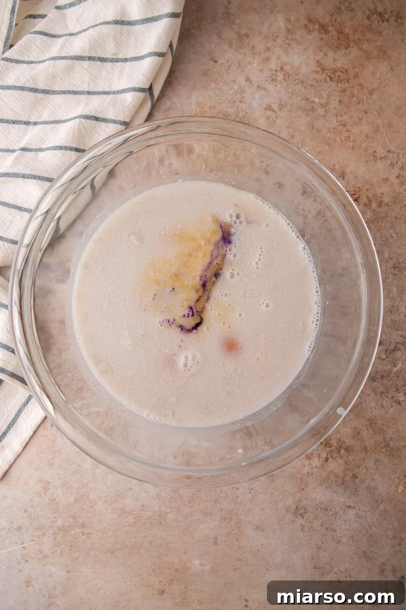Coconut milk custard with eggs, brown sugar, and ube extract in a glass bowl before whisking