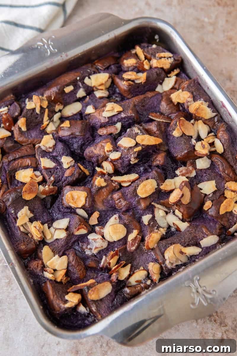 Freshly baked ube French toast bake in a square pan with golden toasted almonds on top