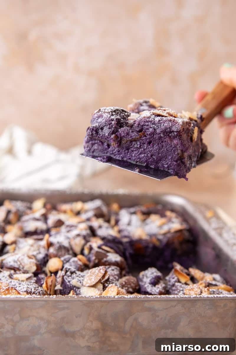 A spatula lifting a slice of ube French toast bake out of the pan revealing the custardy purple interior