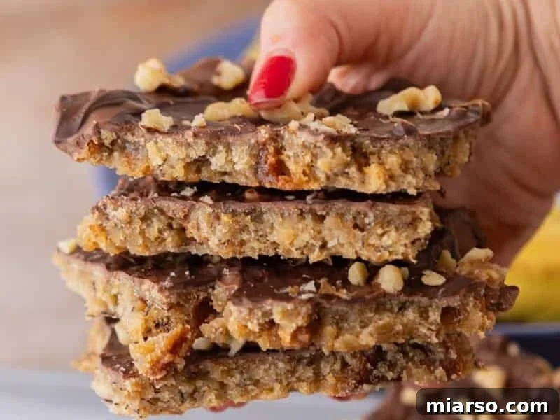 Hand reaching for a stack of banana bread Christmas crack pieces showing layers of chocolate, walnuts, and banana bread.