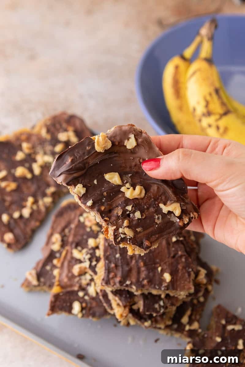 Holding a piece of banana bread Christmas crack topped with chocolate, walnuts, and flaky sea salt.