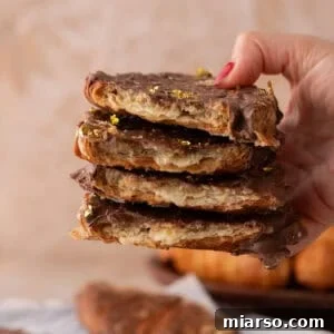 Hand holding a tall stack of croissant Christmas crack pieces with visible flaky layers and gold leaf