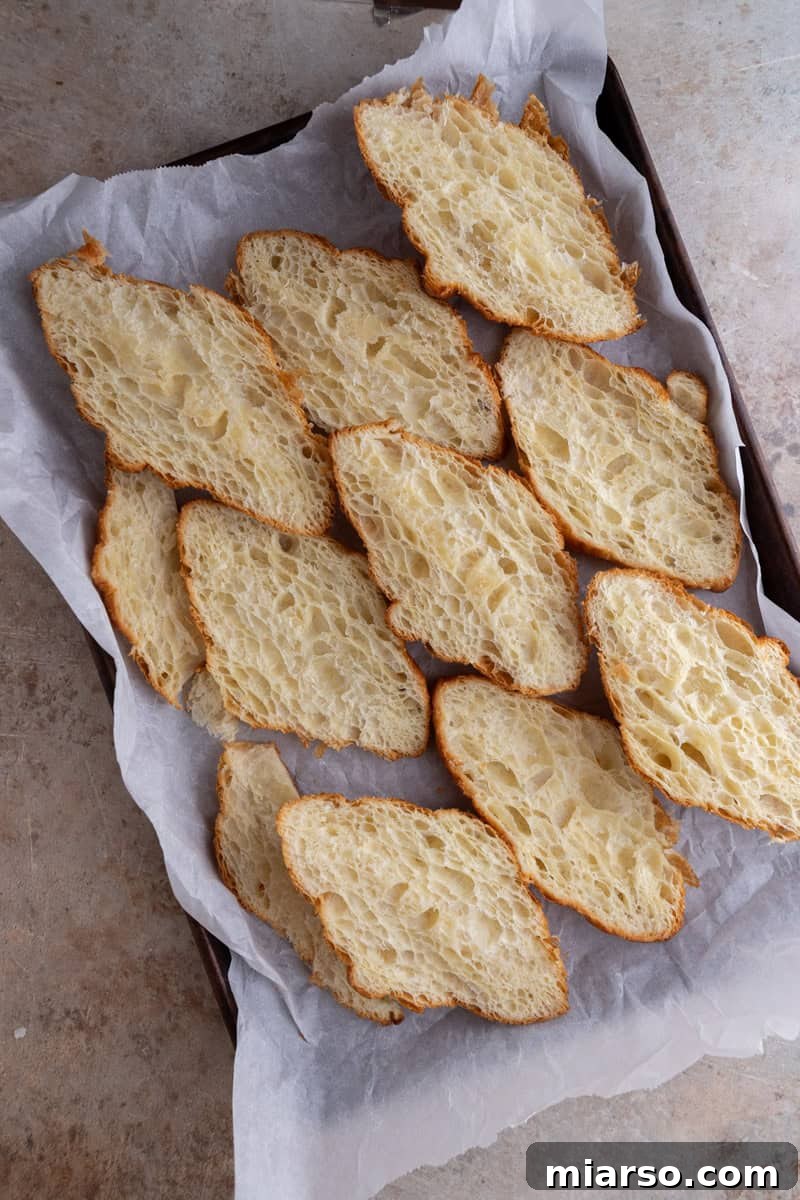 Day-old croissants sliced lengthwise and laid cut side down on a parchment-lined baking sheet