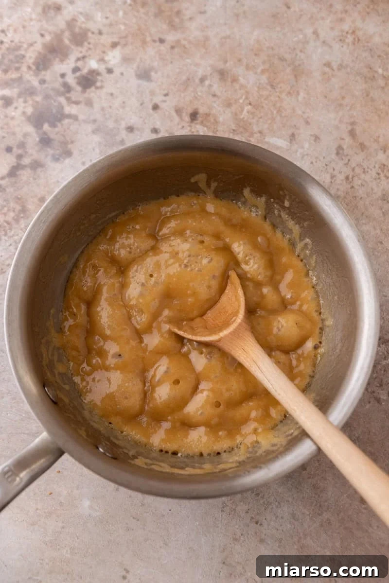 Brown sugar toffee bubbling in a saucepan with a wooden spoon, ready to pour over croissants