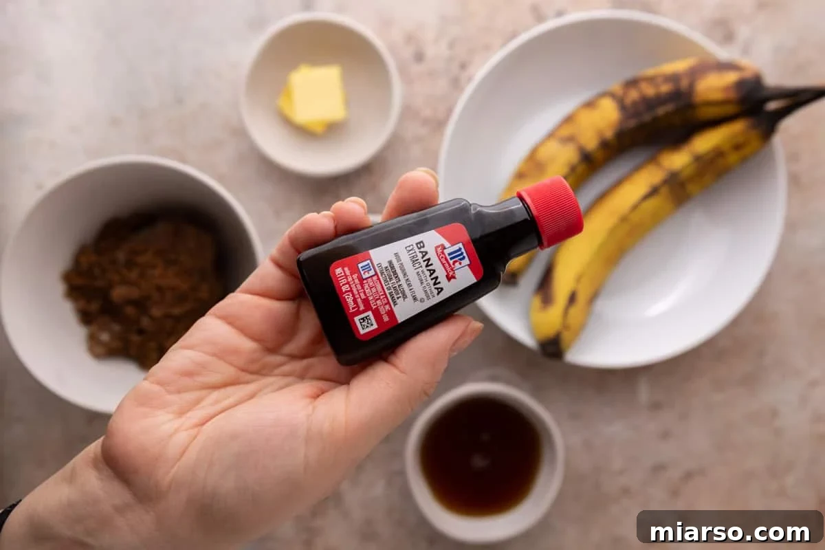 Hand holding a bottle of banana extract over the banana bread syrup ingredients