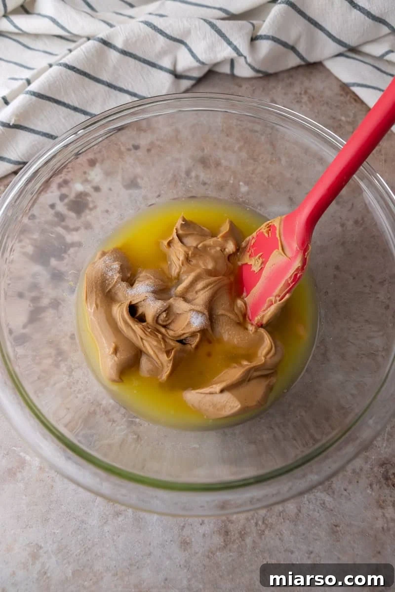 Melted butter and creamy peanut butter in a glass bowl with a red spatula
