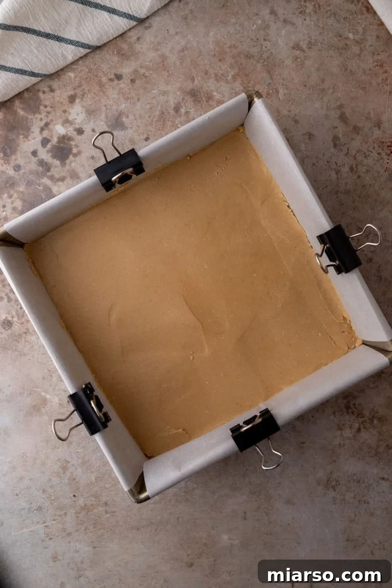 Peanut butter buckeye fudge layer pressed into a parchment lined square pan