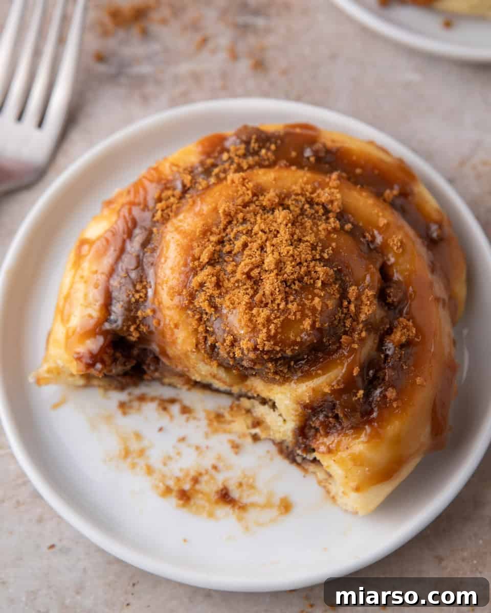 Glazed Biscoff cinnamon roll on a white plate with a bite taken and crushed cookies on top