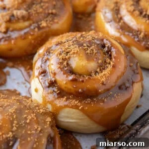 Cookie butter cinnamon roll topped with molten Biscoff glaze dripping down the sides on a sheet pan