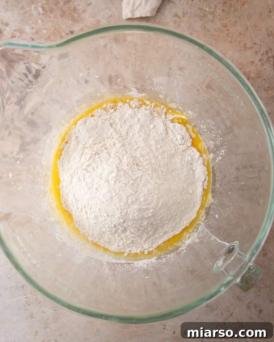  Flour mounded over the wet ingredients in a glass bowl before mixing the cinnamon roll dough