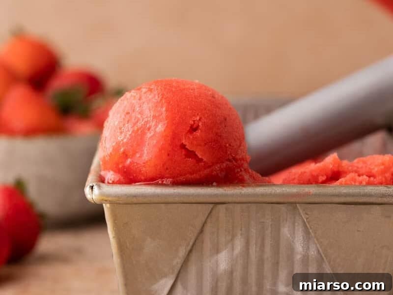 Scoop of bright red strawberry sorbet in a metal loaf pan with fresh strawberries.
