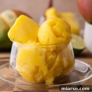 Homemade mango sorbet scoops in a glass dish with fresh mango