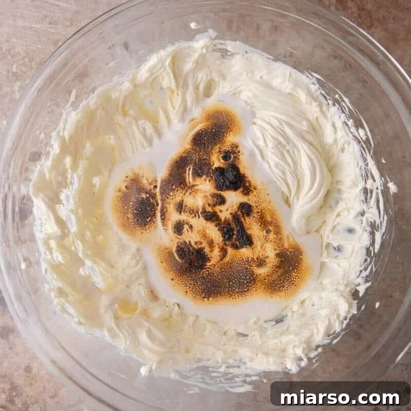 Toasted marshmallow being whipped into beaten cream cheese for the s'mores cheesecake bar filling