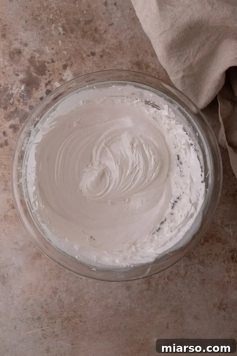Whipped Swiss meringue with glossy stiff peaks in a glass bowl