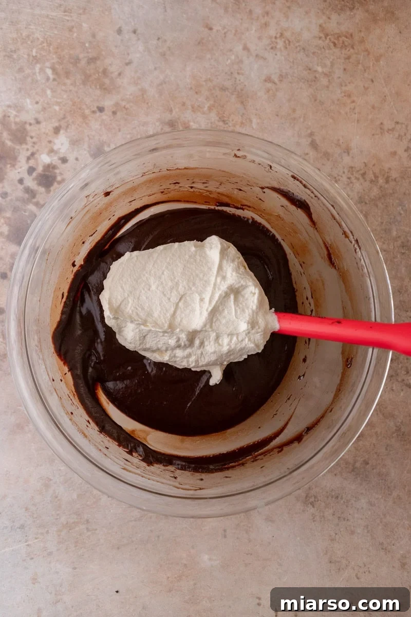 Decadent Chocolate Mousse Cake Recipe 10 First addition of whipped cream being folded into the dark chocolate mixture with a red rubber spatula
