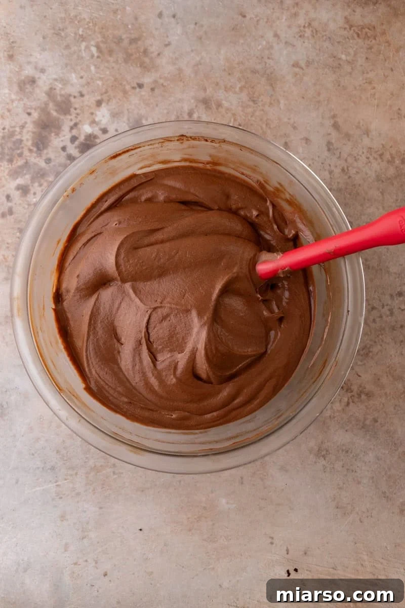 Decadent Chocolate Mousse Cake Recipe 11 Finished chocolate mousse in a glass bowl, smooth and silky with a red rubber spatula