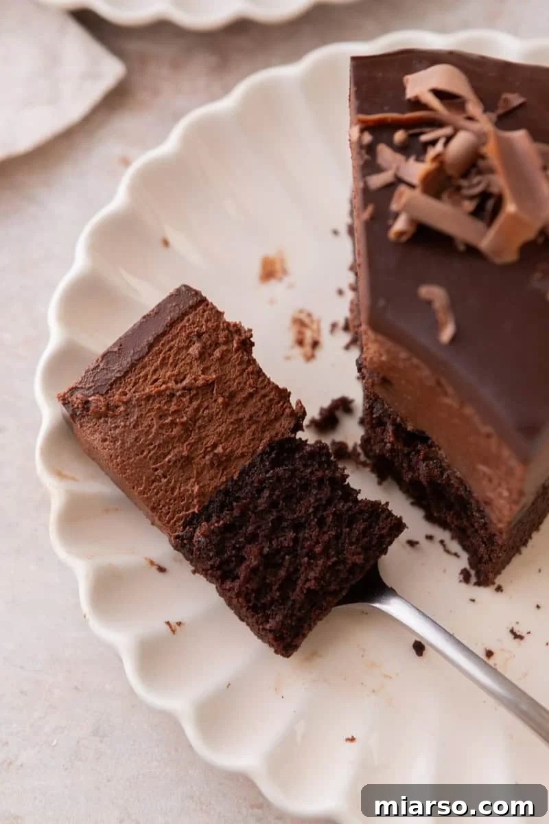 Decadent Chocolate Mousse Cake Recipe 16 A bite taken from a slice of cake on a white scalloped plate, showing the moist cake layer and airy mousse texture up close