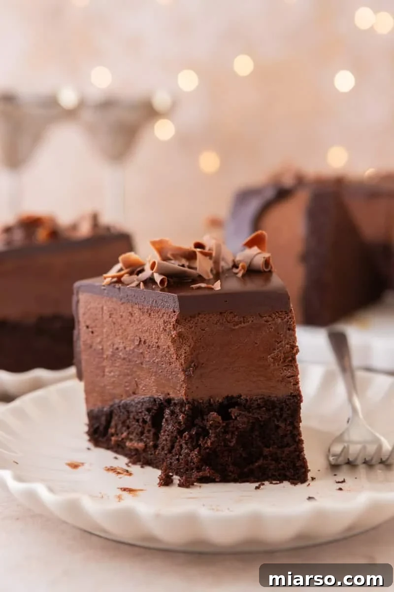 Decadent Chocolate Mousse Cake Recipe 18 A slice of chocolate mousse cake on a plate with a fork, with the rest of the cake and soft bokeh lights in the background