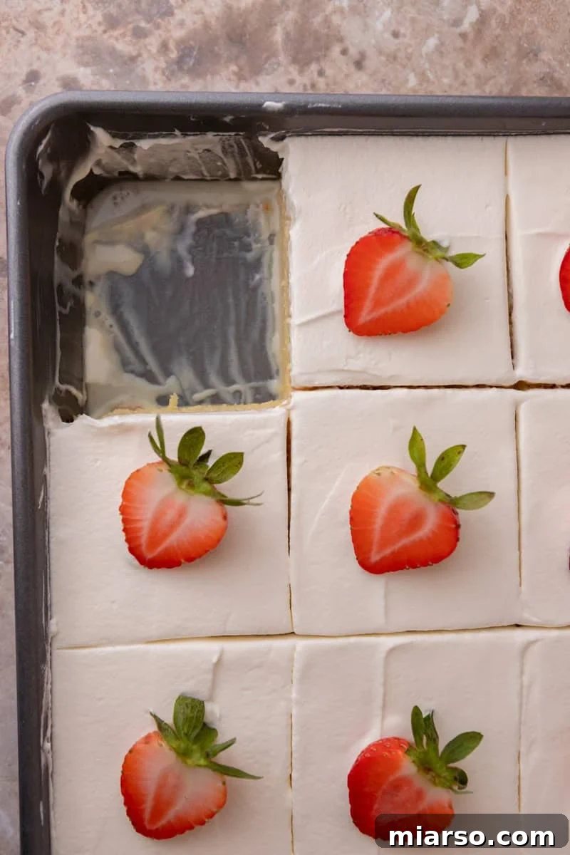 Tres leches cake cut into squares and topped with strawberries in the pan