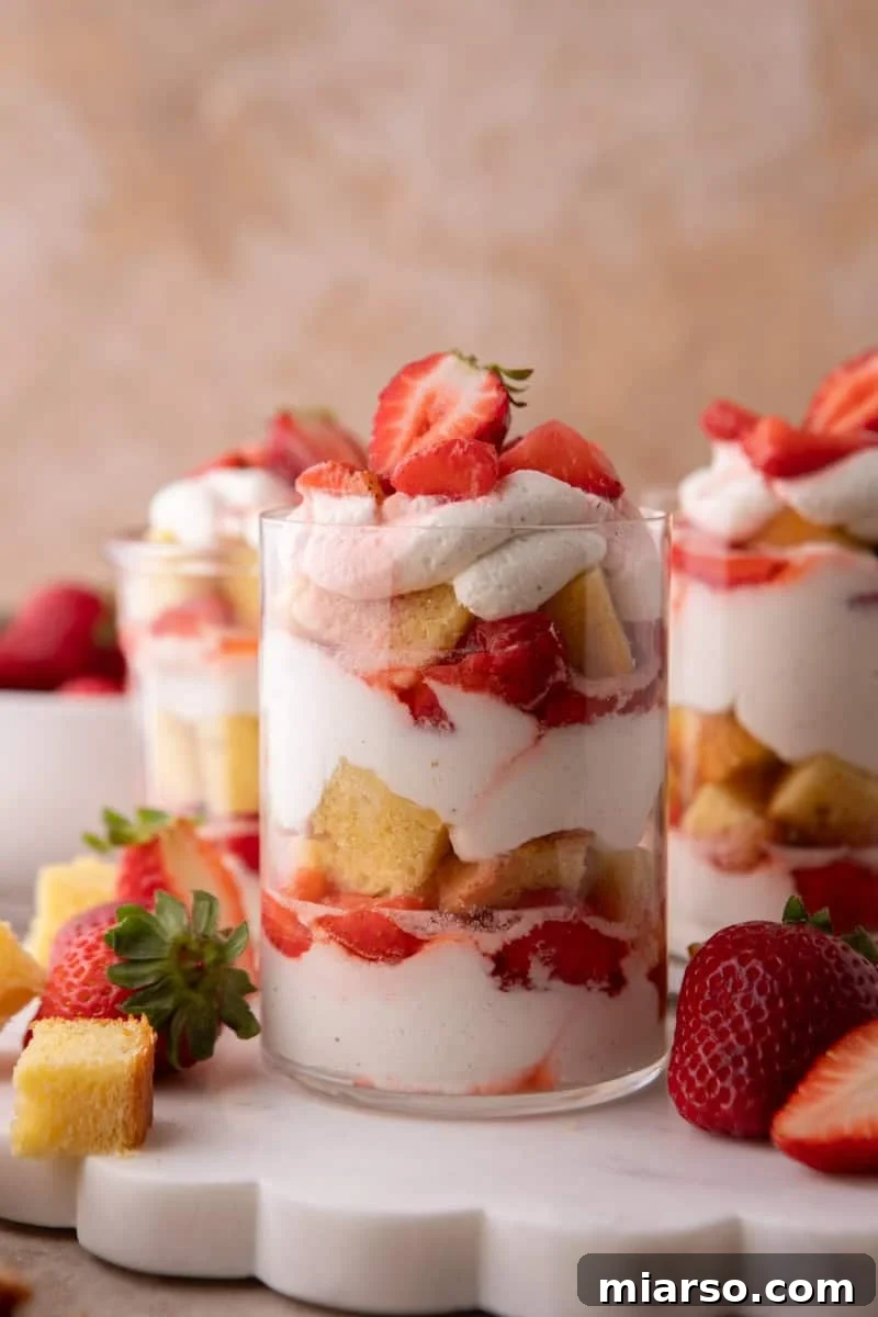 Mini Strawberry Shortcake Trifle Cups Recipe 2 Three strawberry shortcake trifle cups layered with vanilla cake cubes, macerated strawberries, and whipped cream on a marble board.