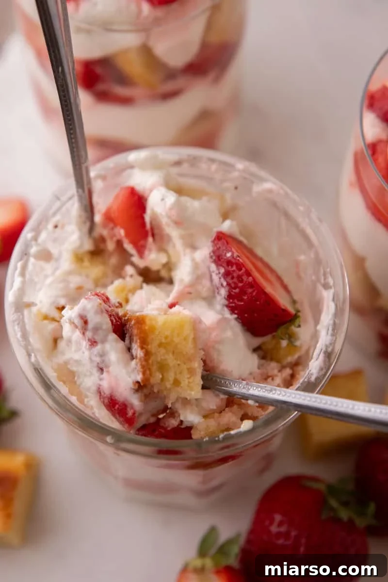 Mini Strawberry Shortcake Trifle Cups Recipe 10 Overhead view of a spoon digging into a strawberry shortcake trifle cup with visible cake cubes and berries