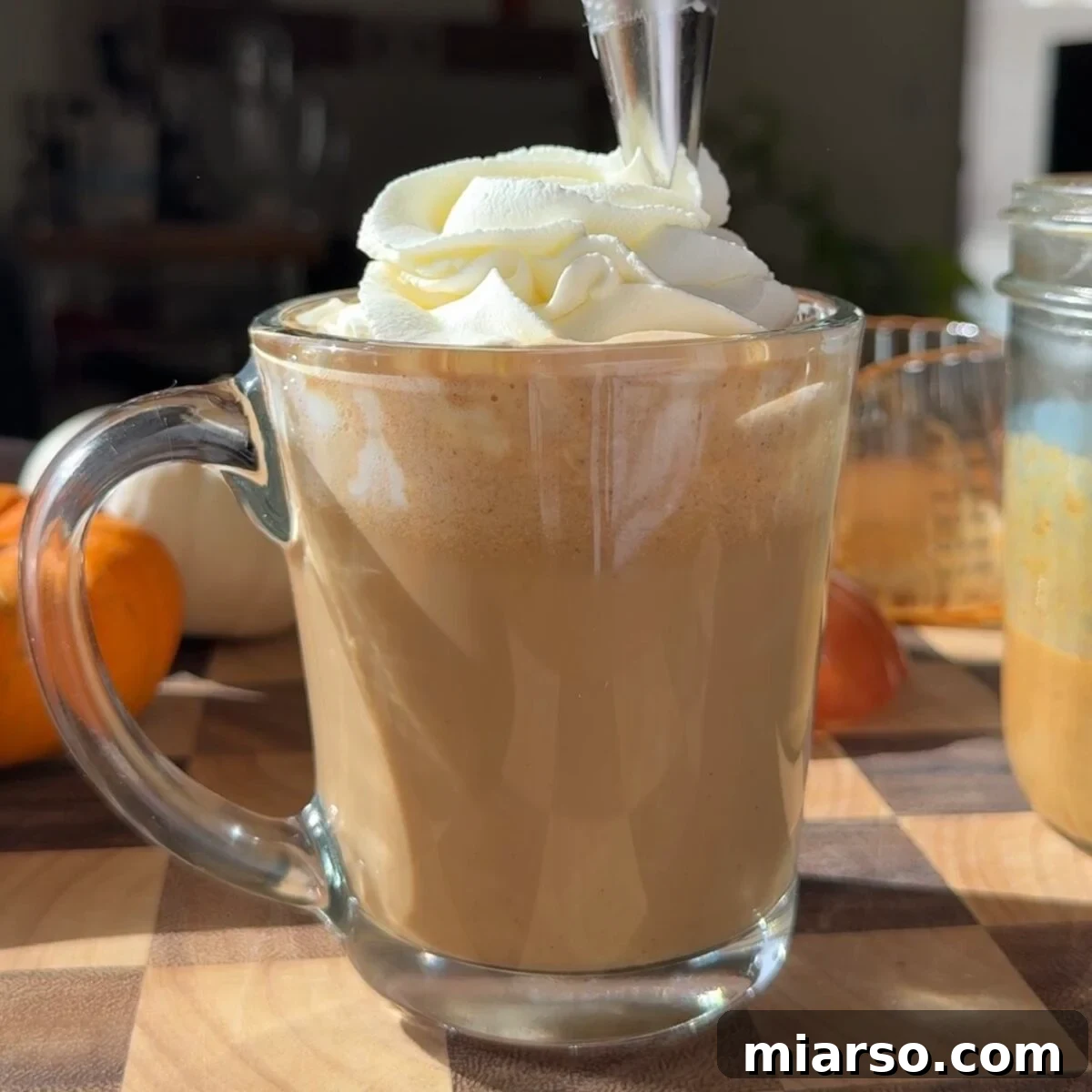 Make a Copycat Starbucks Pumpkin Spice Latte at Home 7 Whipped cream being piped on top of a pumpkin spice latte in a glass mug.